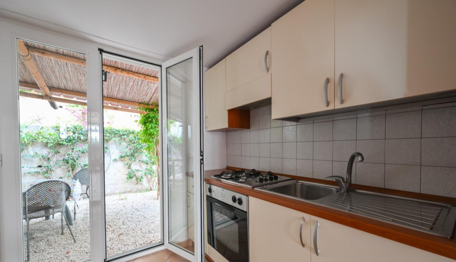 Cucina con porta aperta su giardino, piano cottura e lavello.