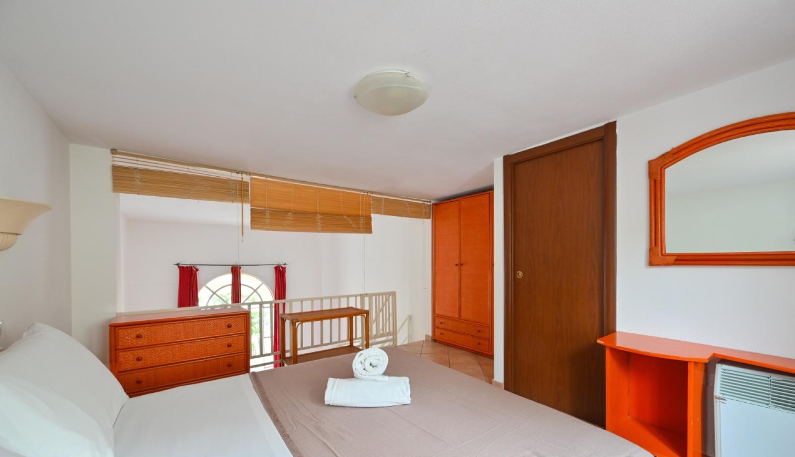 Camera da letto con mobili in legno, letto matrimoniale e specchio a parete.