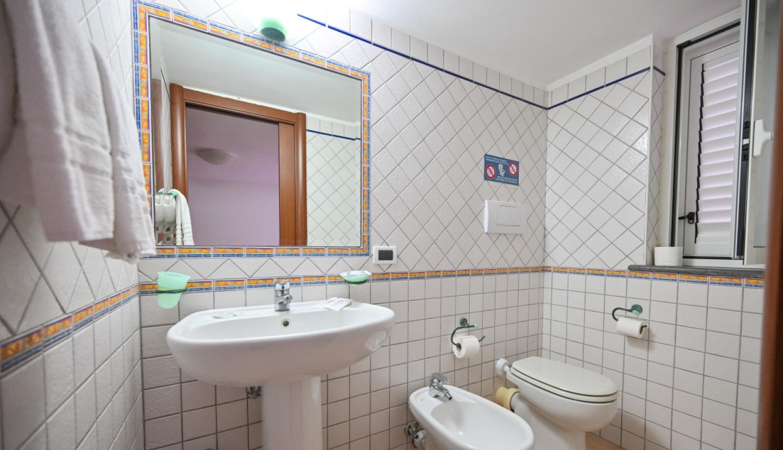 Bagno con lavabo, bidet, WC, specchio e piastrelle bianche decorate.