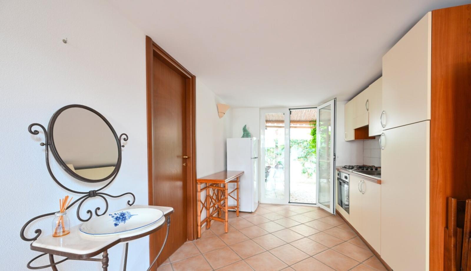 Cucina luminosa con mobili chiari, specchio decorativo e accesso al giardino.