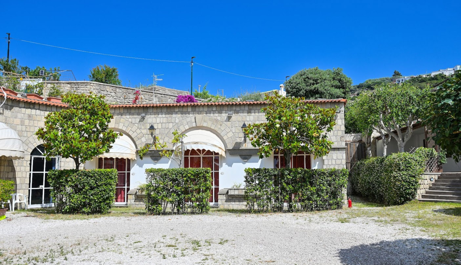 Edificio in pietra con giardino, alberi e cielo blu sullo sfondo.