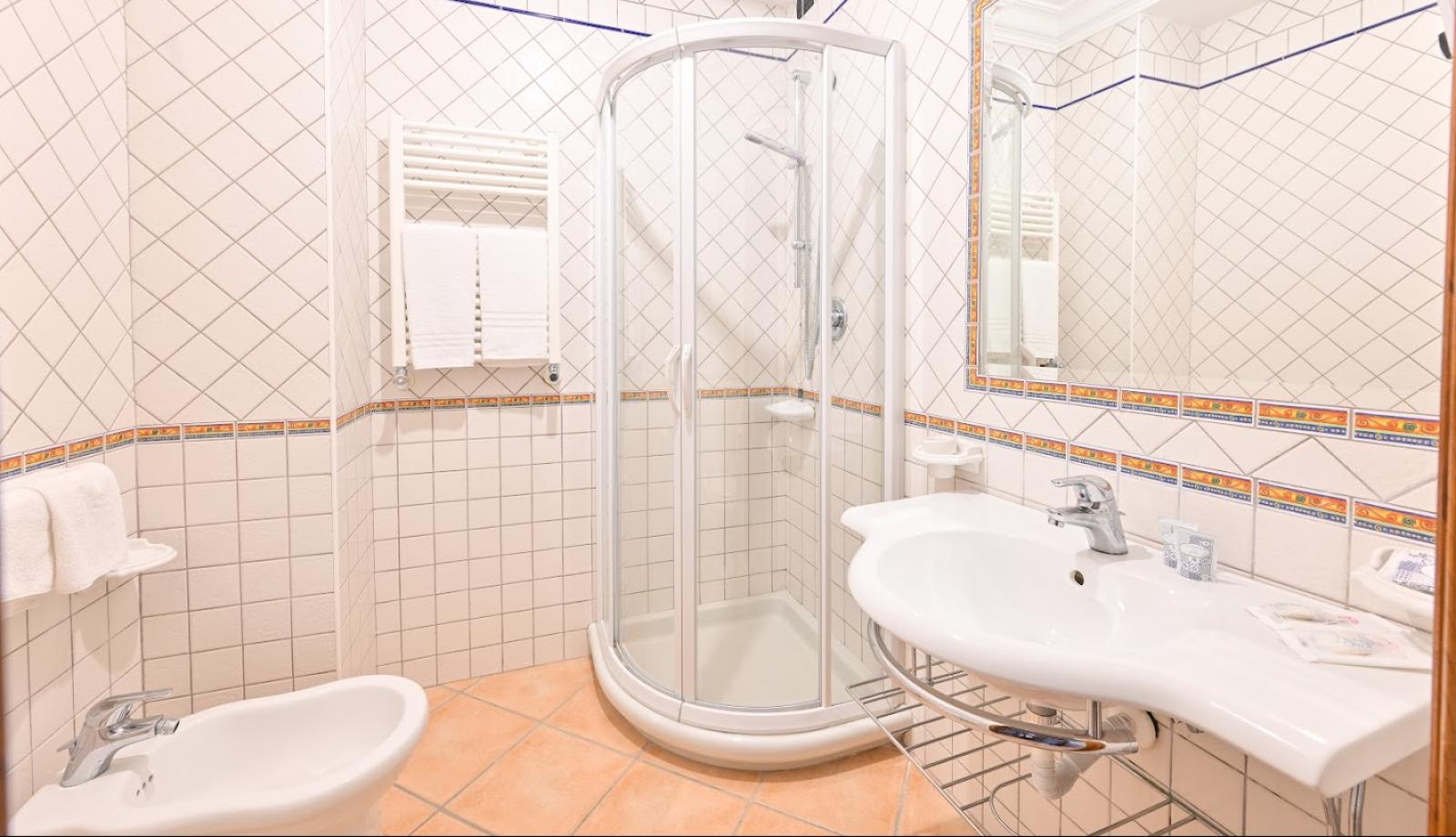 Bagno con doccia angolare, bidet e piastrelle bianche con dettagli colorati.