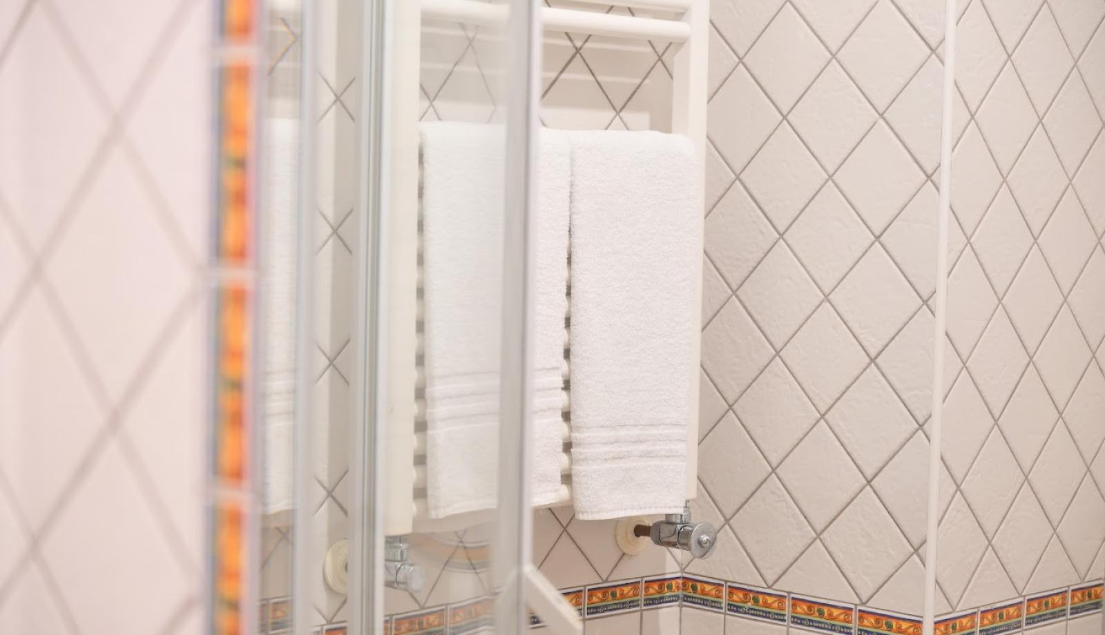 Bagno con piastrelle bianche, asciugamani bianchi su scaldasalviette e bordo decorativo colorato.