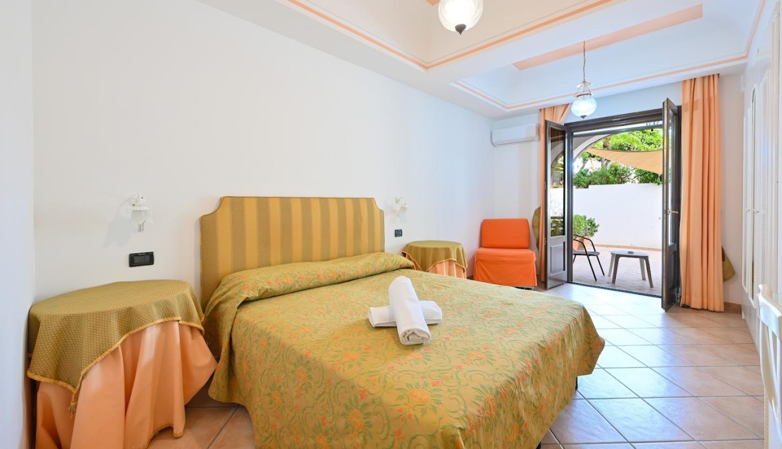Camera luminosa con letto matrimoniale, terrazza e arredamento dai toni caldi.
