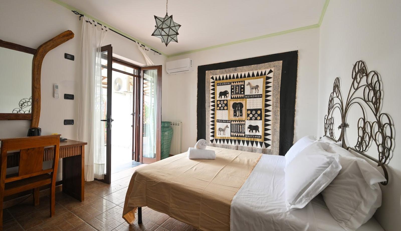 Camera accogliente con decorazioni africane, letto matrimoniale e accesso al balcone.