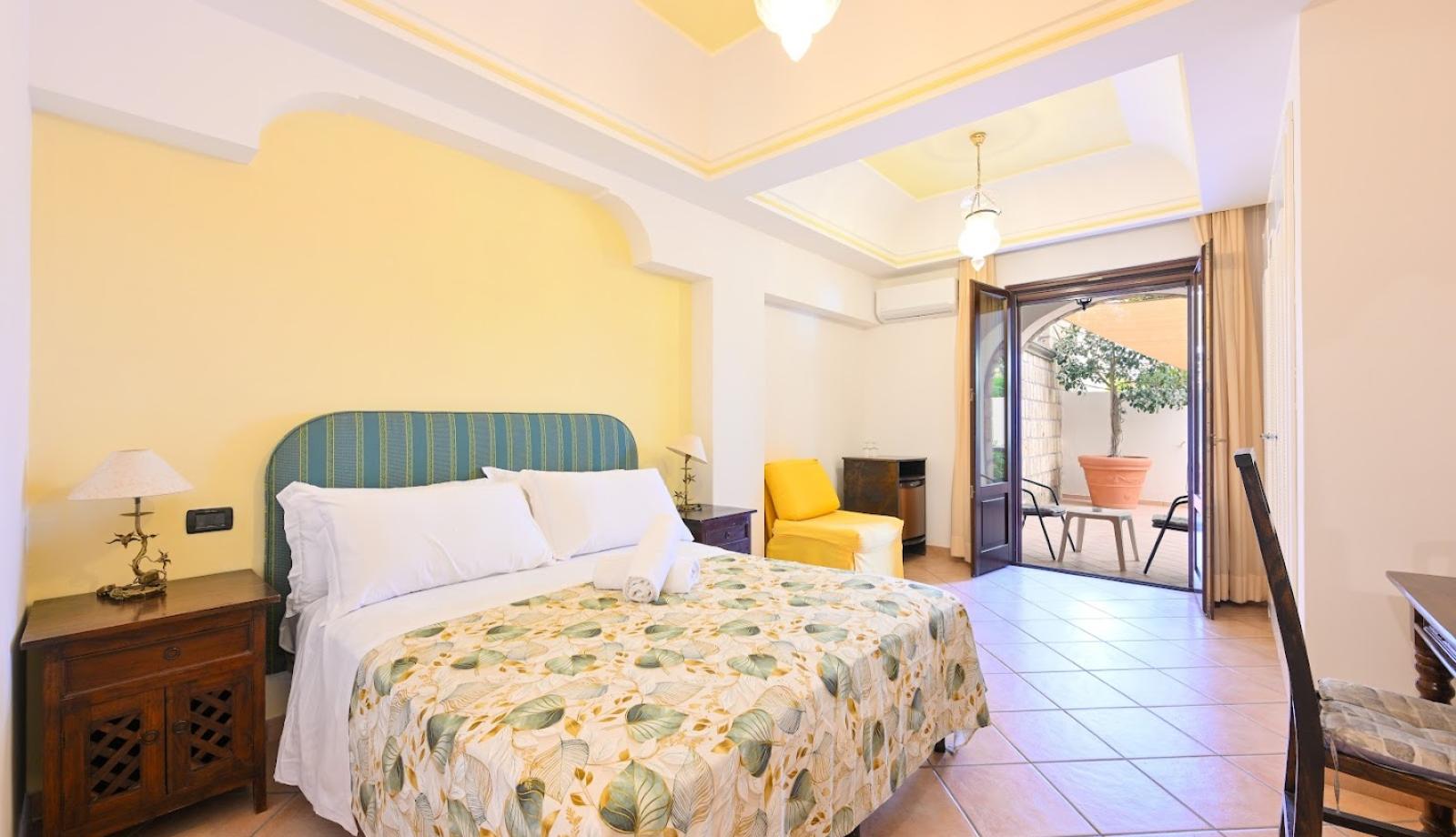 Camera luminosa con letto matrimoniale, arredi eleganti e accesso al patio esterno.