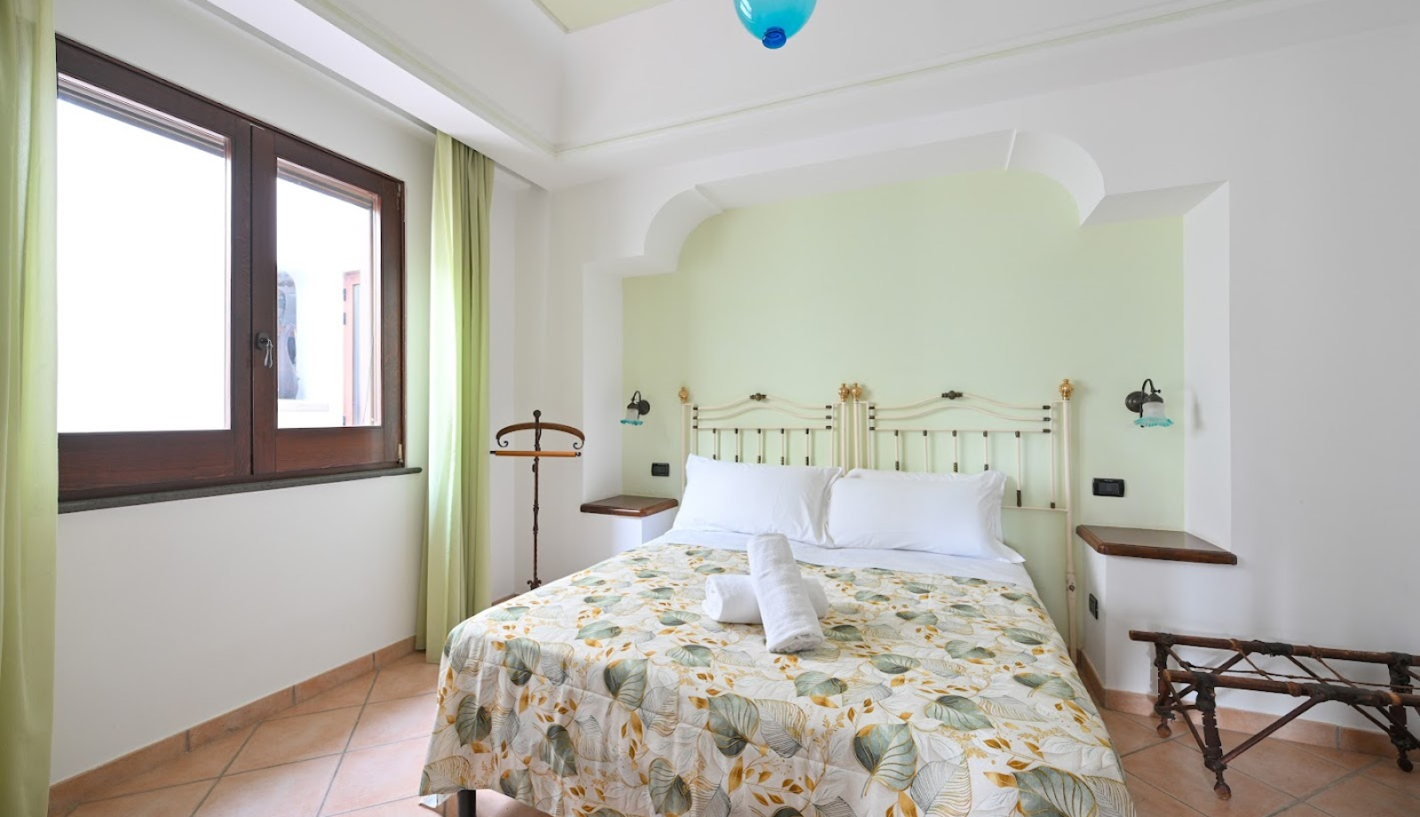 Camera da letto luminosa con letto matrimoniale, pareti chiare e decorazioni naturali.