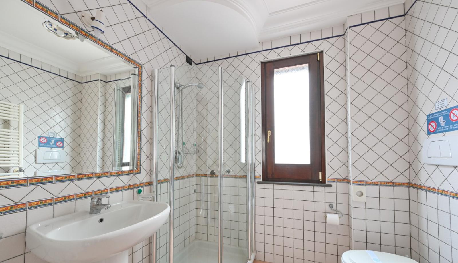 Bagno moderno con doccia, lavabo, WC, piastrelle bianche e dettagli colorati.