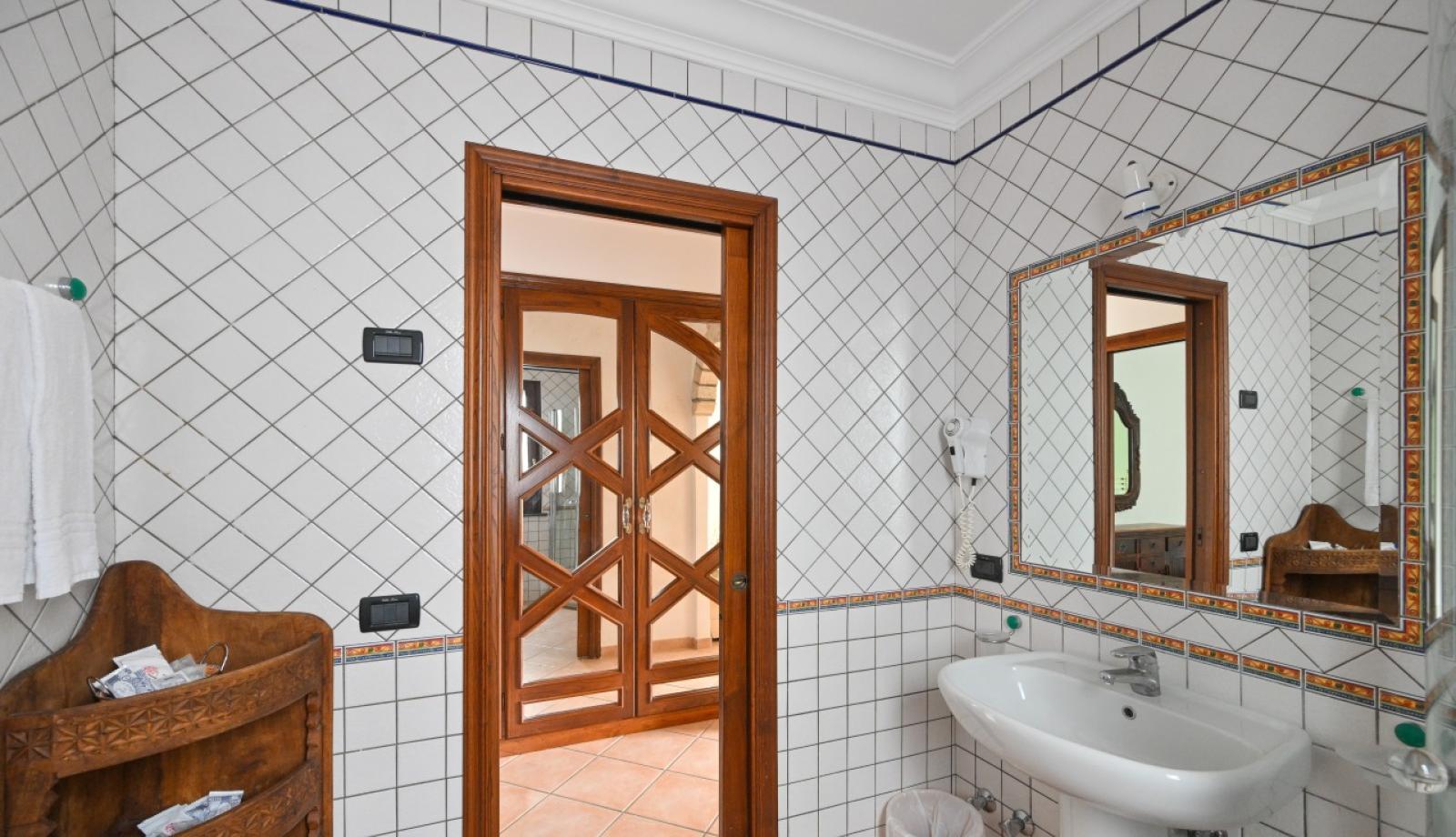 Bagno con piastrelle bianche, specchio grande e porta in legno intagliato.
