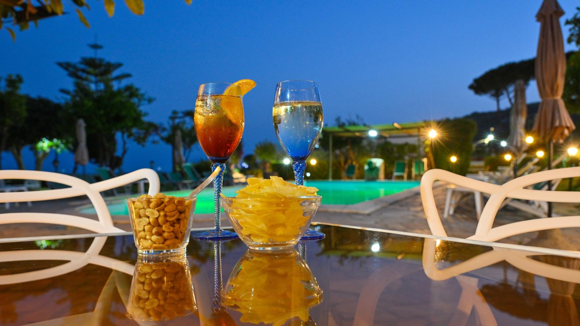 Aperitivo a bordo piscina con cocktail, patatine e arachidi al tramonto.