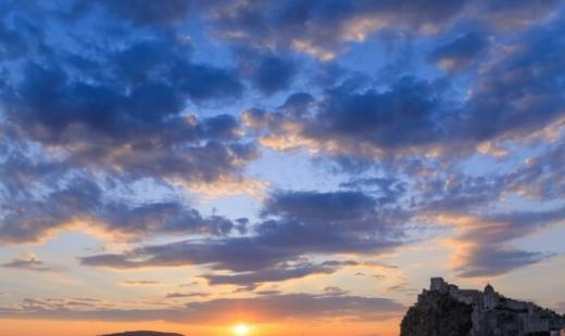 Tramonto sul mare con castello e barche all'orizzonte.