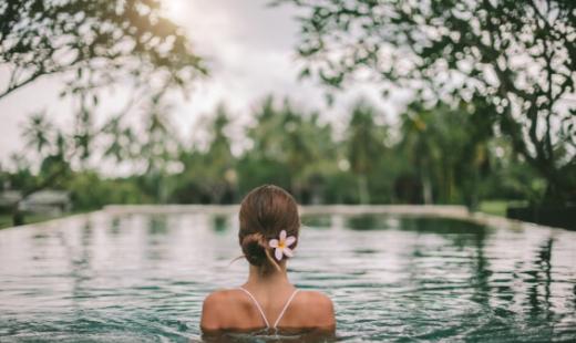 Donna in piscina con fiore tra i capelli, immersa nella natura tropicale.