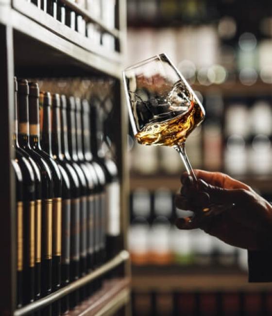 Calice di vino bianco in una cantina tra scaffali di bottiglie.