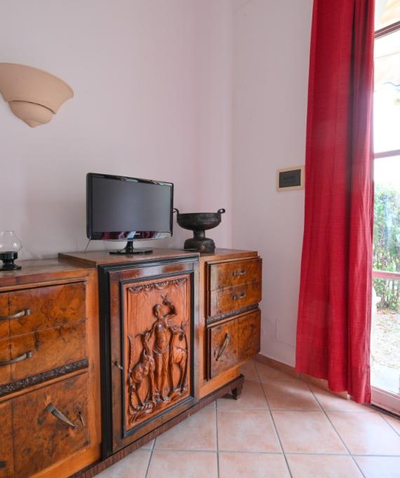 Mobile antico con TV, tende rosse e porta finestra su giardino.