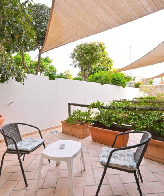 Terrazza con sedie, tavolo, piante in vaso e vele ombreggianti.