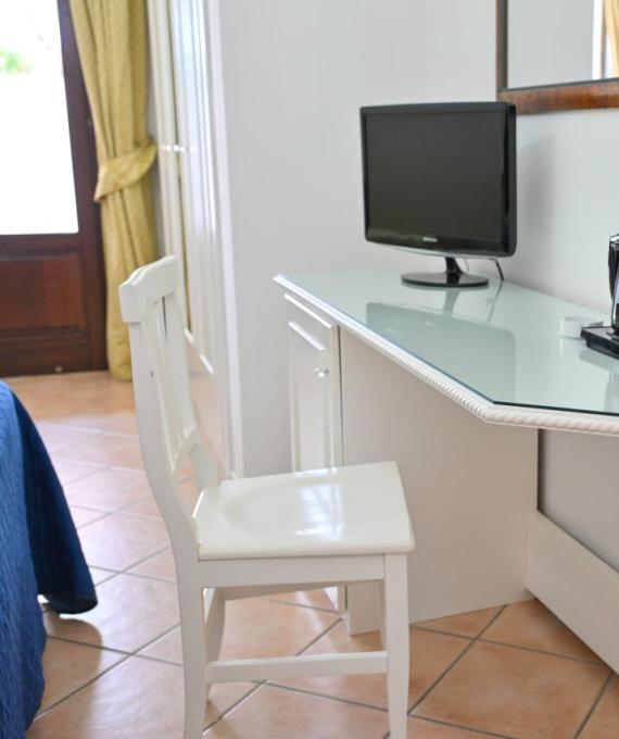 Scrivania con TV, bollitore, tazza e sedia in una stanza luminosa.