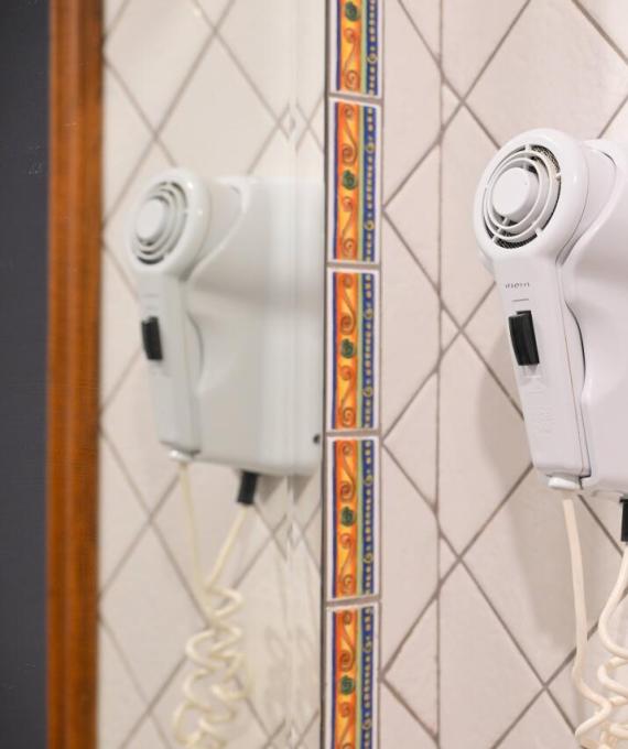 Asciugacapelli bianco montato a parete con piastrelle decorative e specchio riflettente.