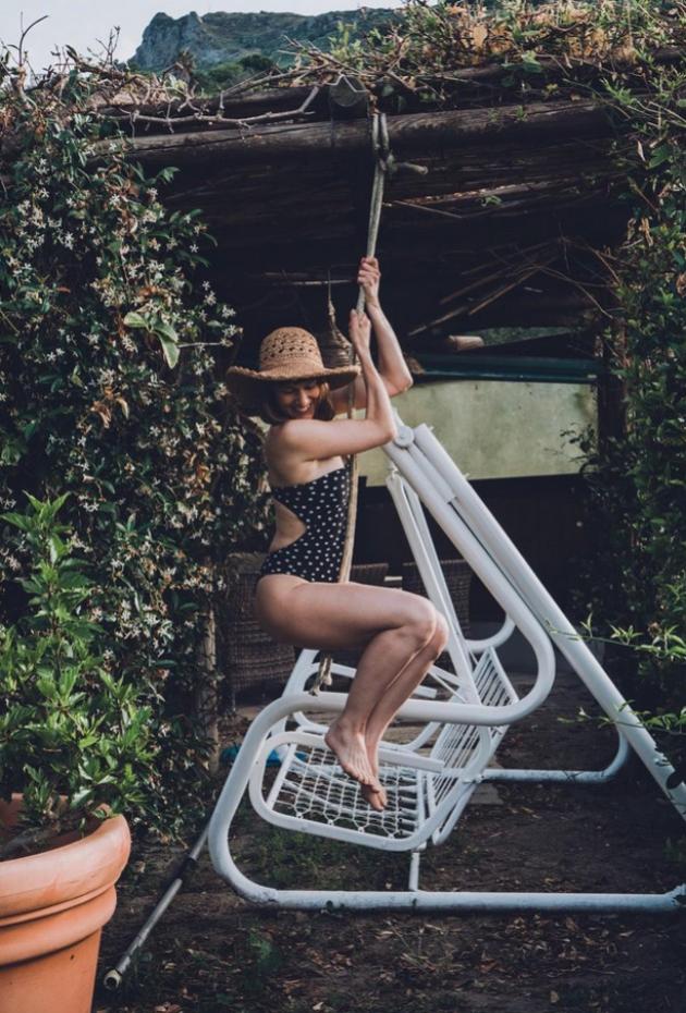 Donna su altalena bianca, indossa costume a pois e cappello di paglia.