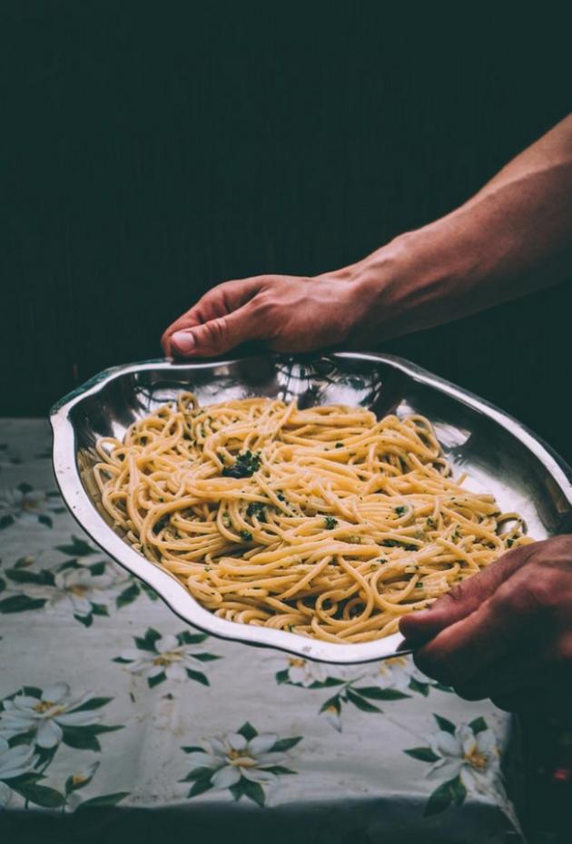Piatto di spaghetti con prezzemolo su vassoio d'argento, tenuto da mani robuste.