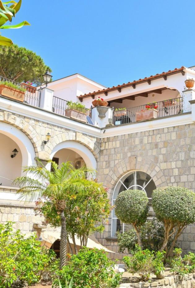 Villa mediterranea con terrazza, archi in pietra e giardino curato.