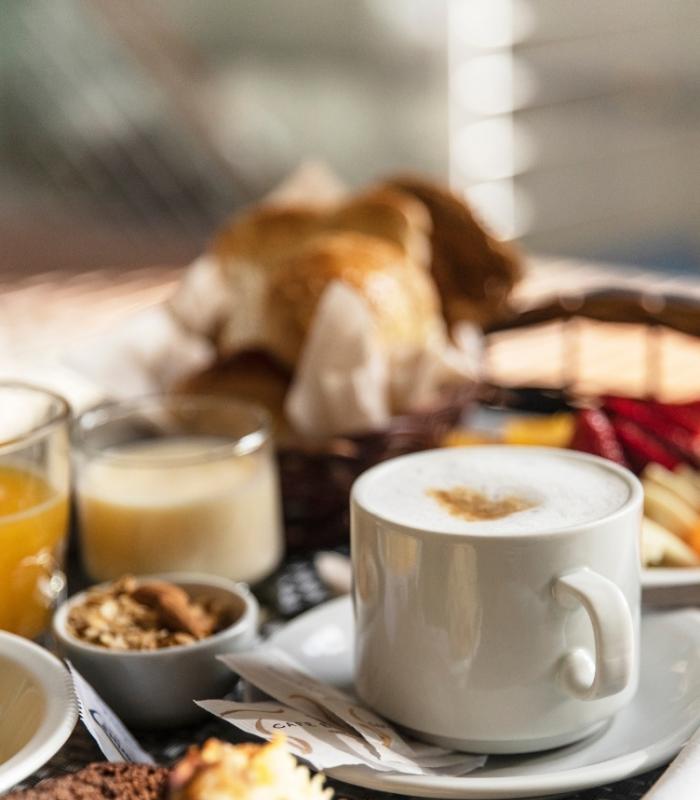 Colazione con cappuccino, succo d'arancia, dolci e cereali in un cestino.