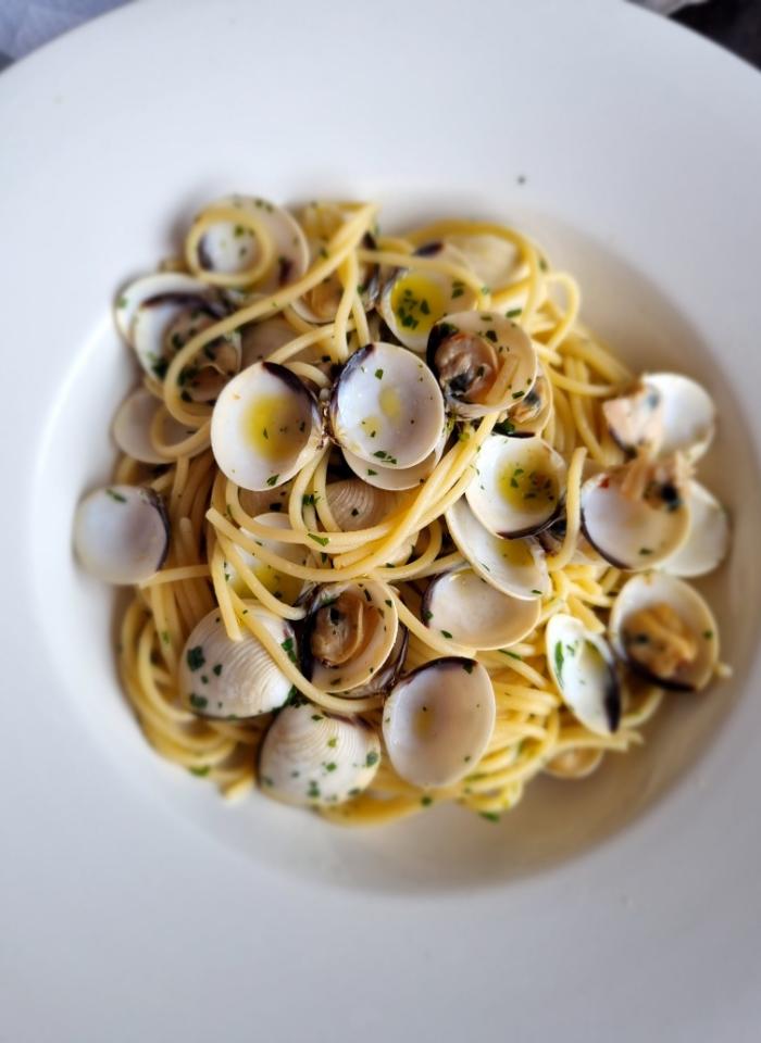 Spaghetti alle vongole con prezzemolo e olio d'oliva su piatto bianco.