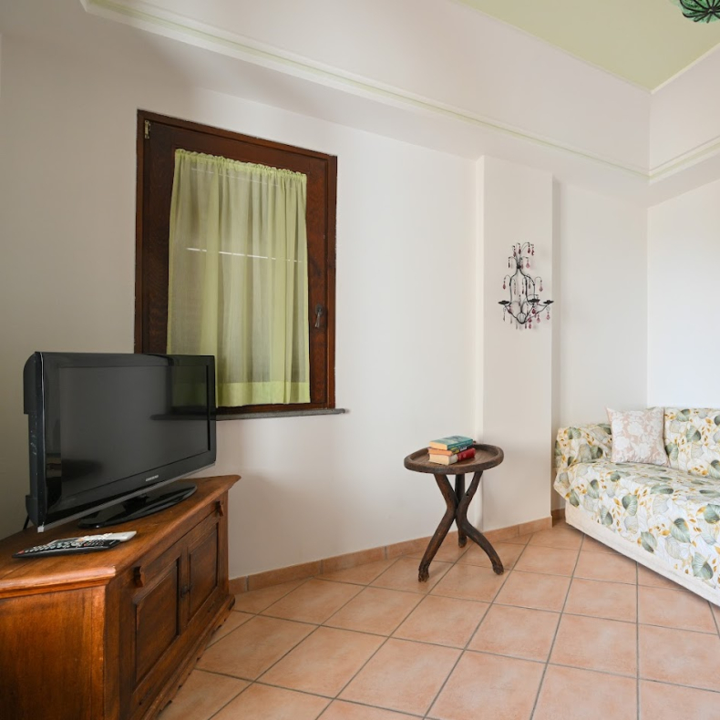 Soggiorno accogliente con divano floreale, TV e tavolino in legno.